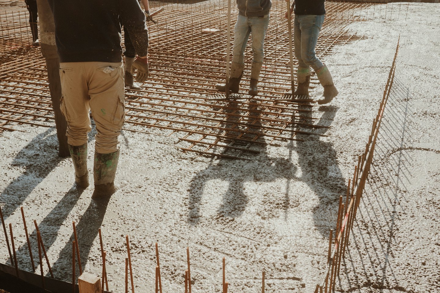 Construction workers level wet concrete over a steel rebar grid.