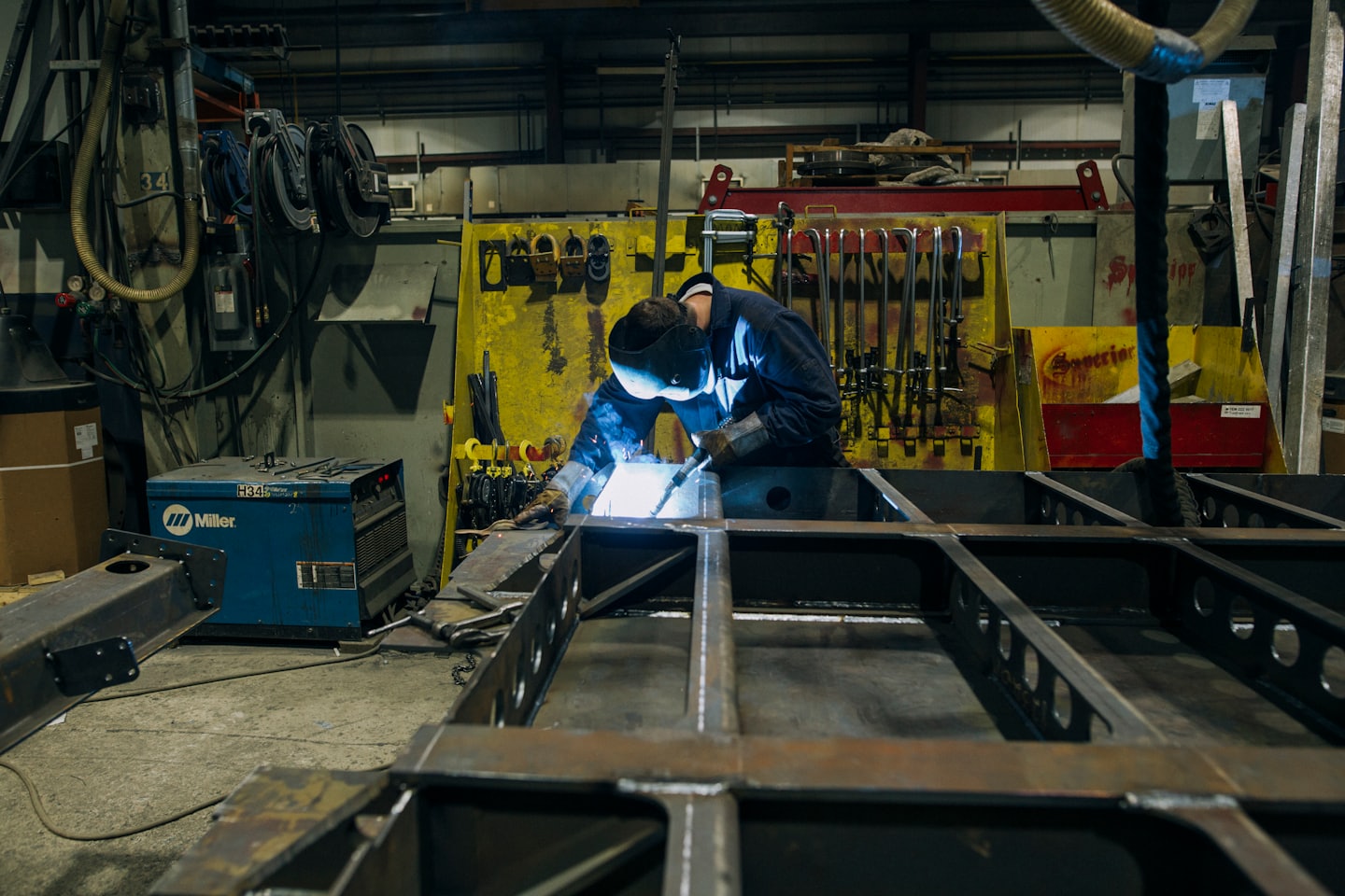 Welder in helmet and gloves sparks metal frame in workshop.
